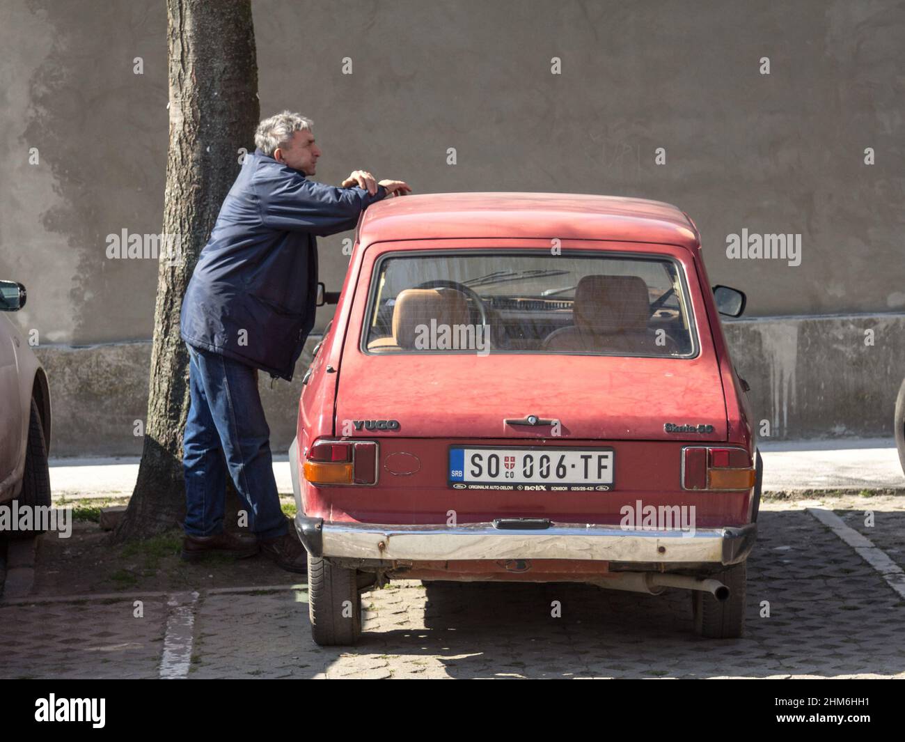 Picture of a Skala car, red colors, branded as Zastava 55 and Yugo 55, parked in a car park of Sombor Serbia with an old man standing on it. Skala is Stock Photo