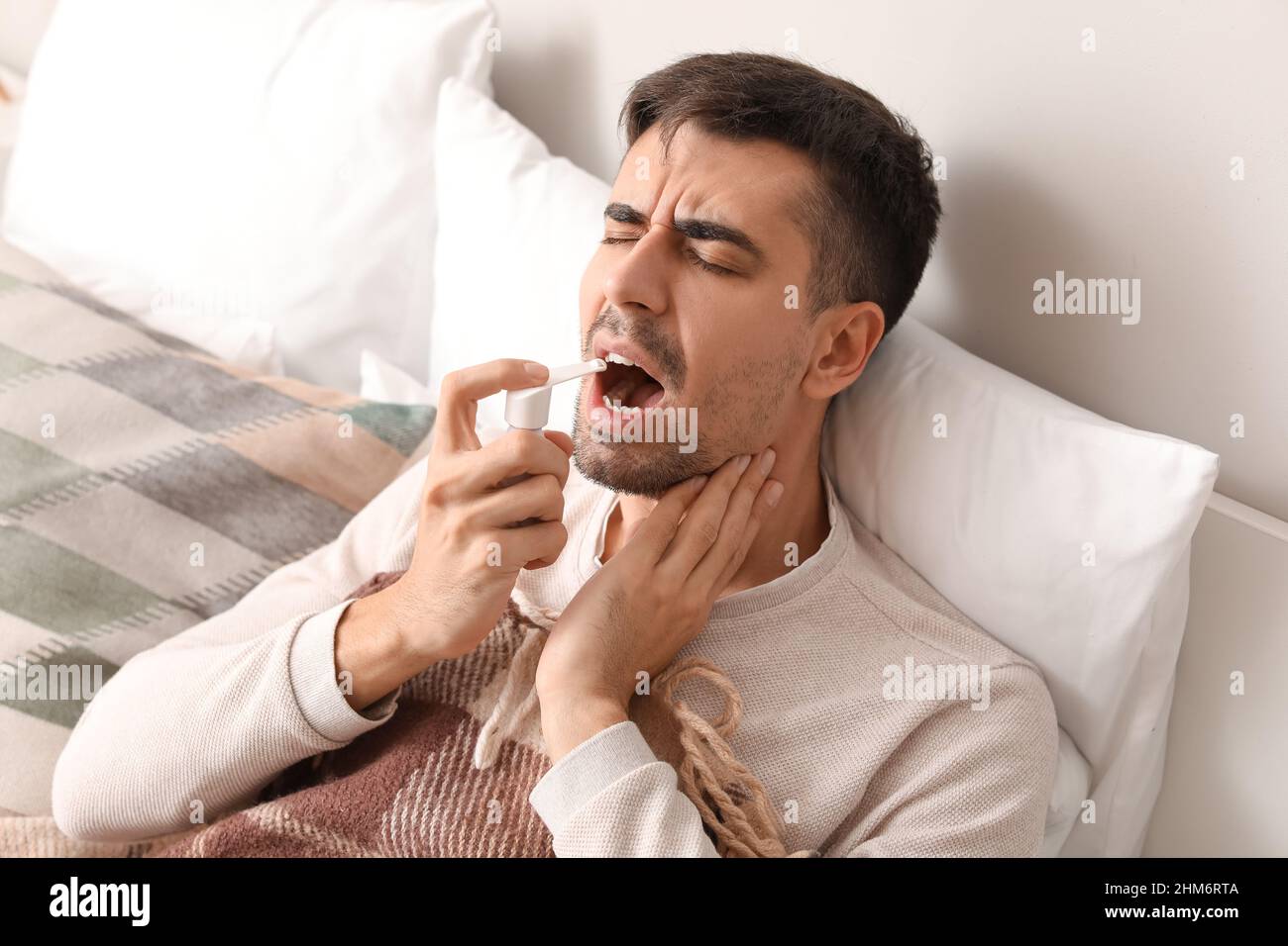 Ill young man with sore throat using inhaler in bed Stock Photo Alamy