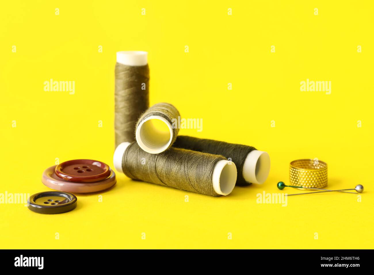 Sewing thread spools, pins, thimble and buttons on color background Stock Photo