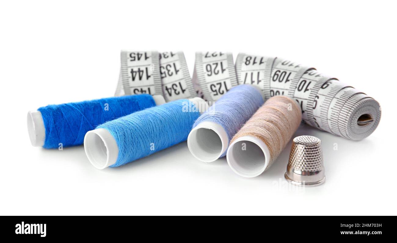 Thread spools, measuring tape and thimble on white background Stock Photo