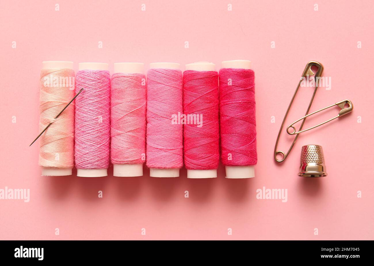 Multicolored thread spools, safety pins and thimble on color background Stock Photo