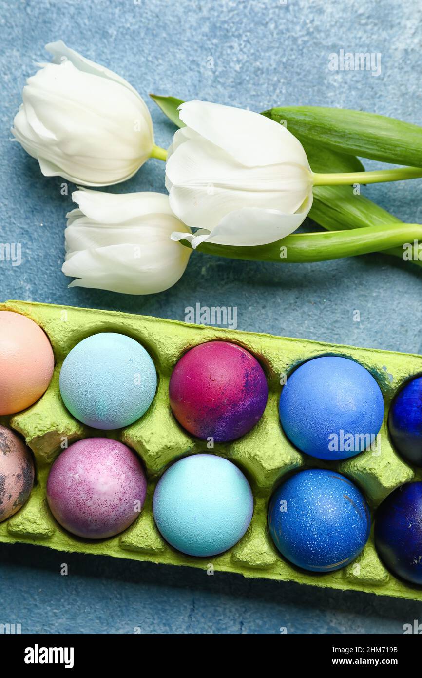 Holder with painted Easter eggs and tulips on color background Stock ...