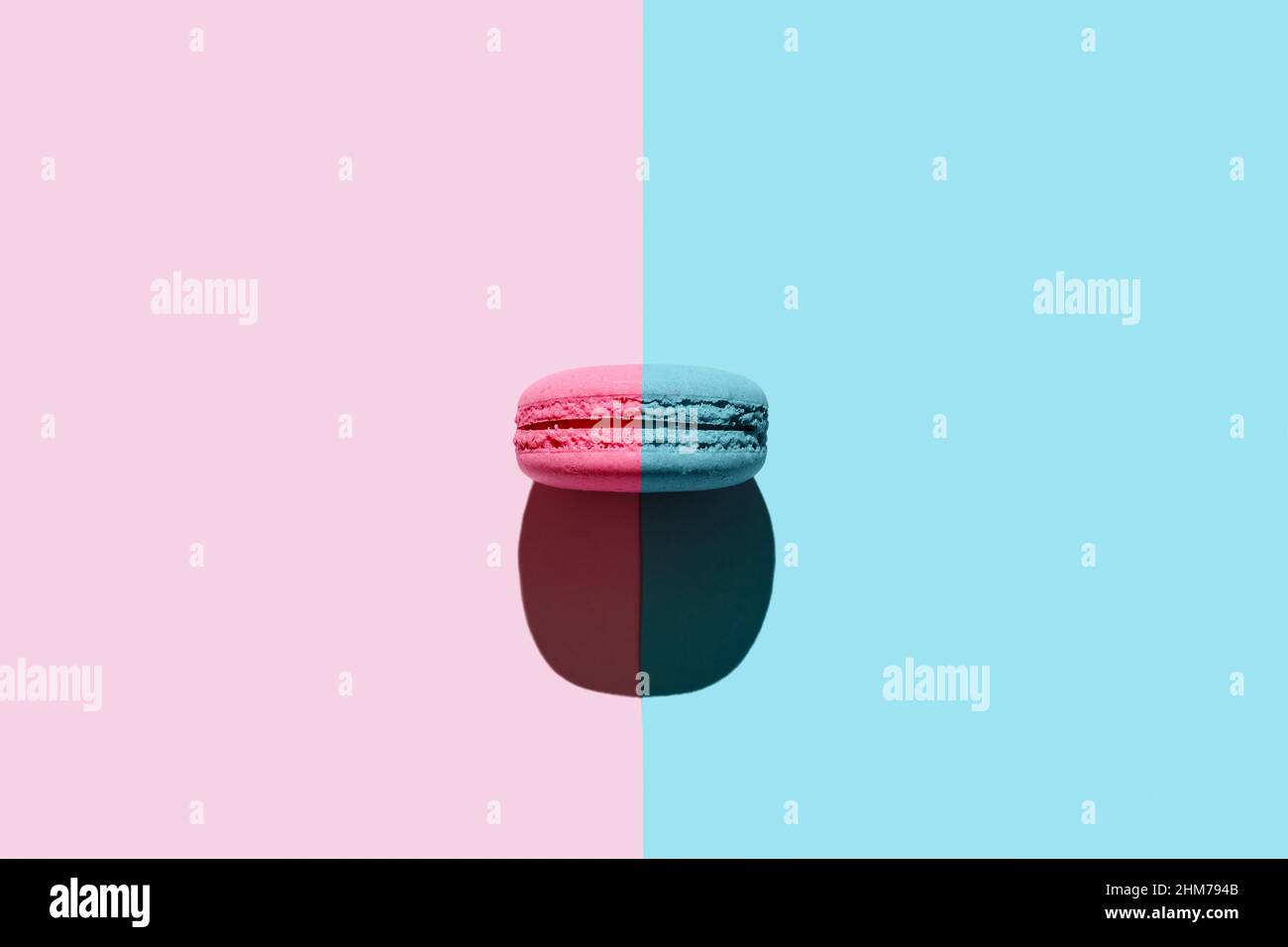 One macaroon with creative layout. Two colors duotone macaron with pink and blue background. Top view with hard light. Stock Photo