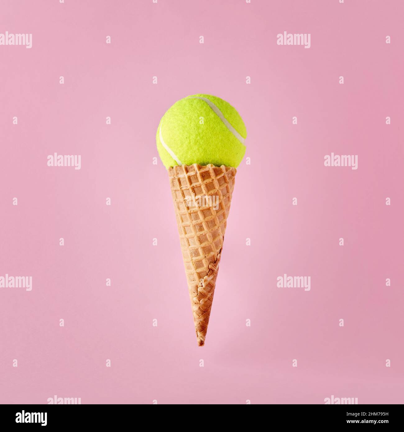 Tennis ball on ice cream cone on pink background. Minimalistic sports, fun and recreation concept. Stock Photo