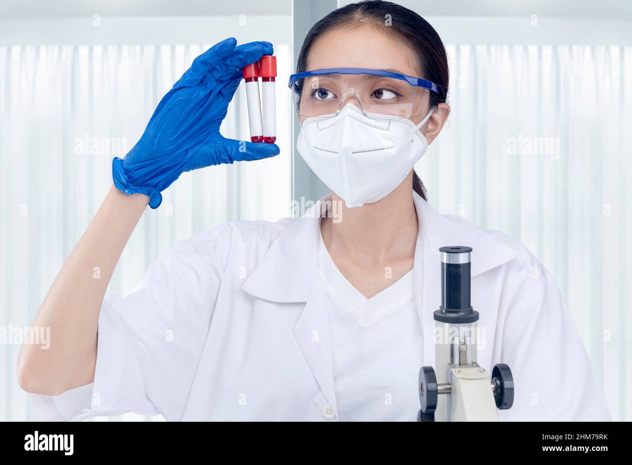 Asian researcher woman with face mask and glasses holding medical tube on the lab Stock Photo