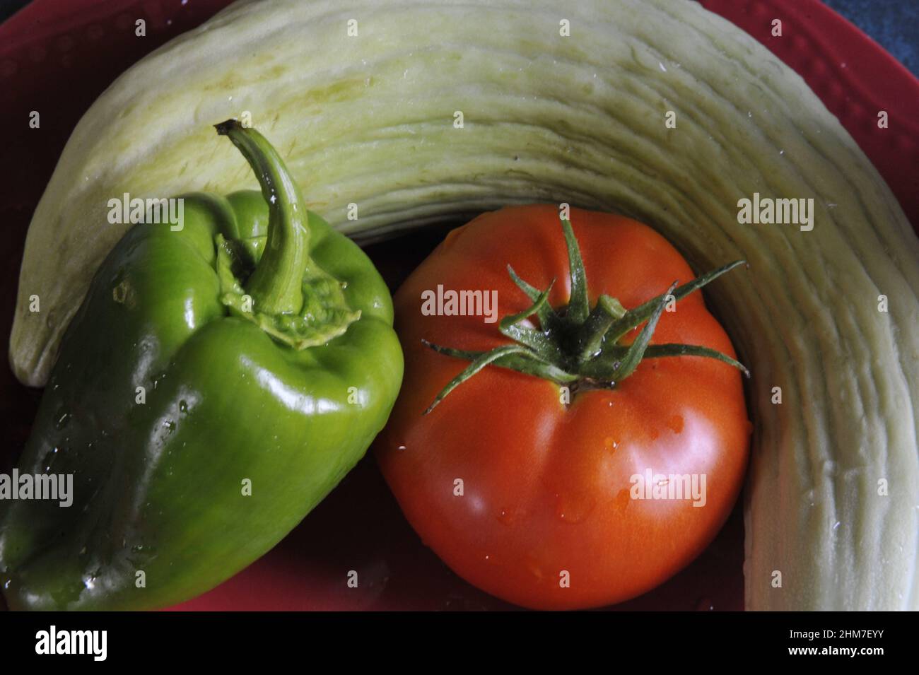 Close-up top view of freshly picked green pepper, tomato and zucchini in a red bowl Stock Photo