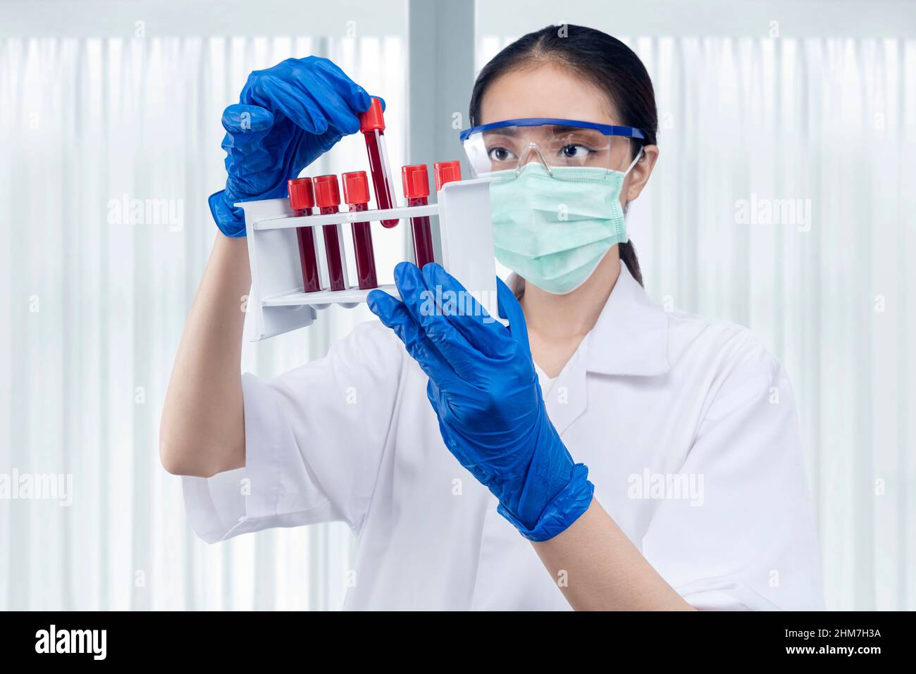 Asian researcher woman with face mask and glasses holding medical tube rack on the lab Stock Photo