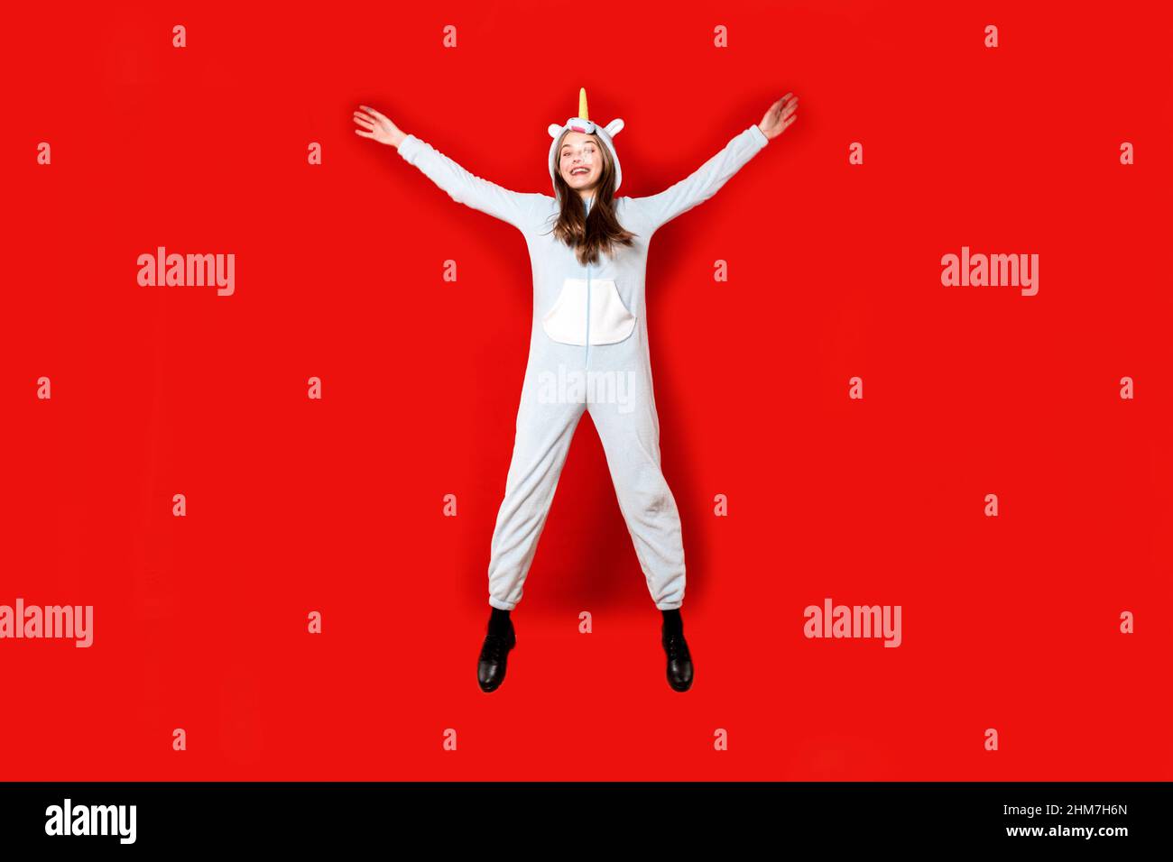 Girl in unicorn pajamas on a red background is jumping. Overnight stay