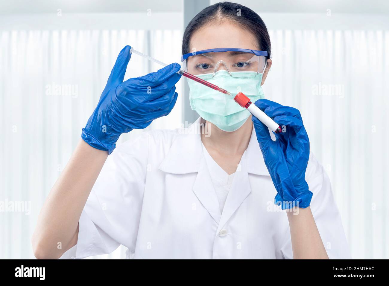Asian researcher woman with face mask and glasses taking a sample from the medical tube on the lab Stock Photo