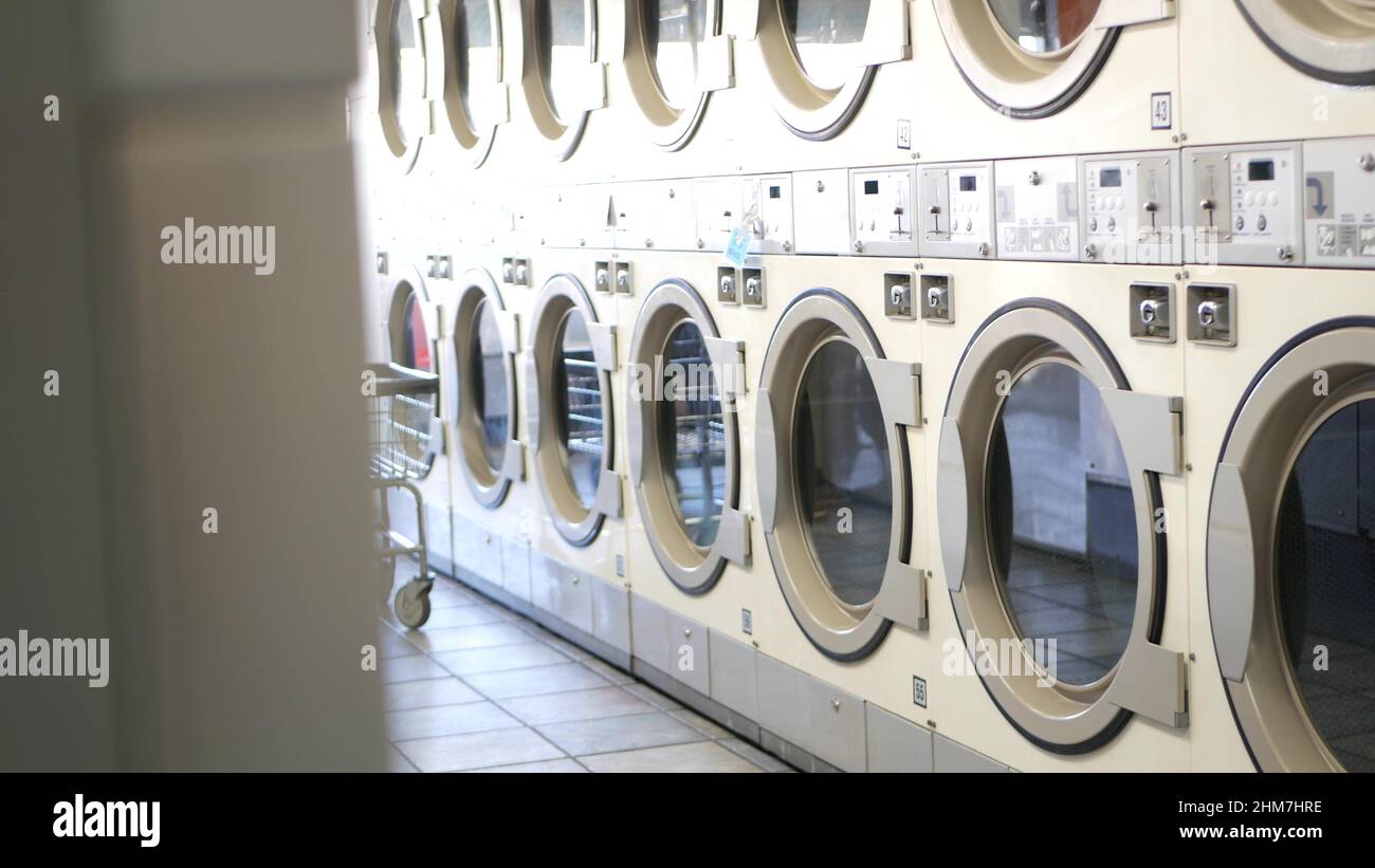 Row of washing and drying machines, public coin laundry in California, USA. Drums of washers and dryers in self-service laundromat or commercial laundrette. Automatic launderette in United States. Stock Photo
