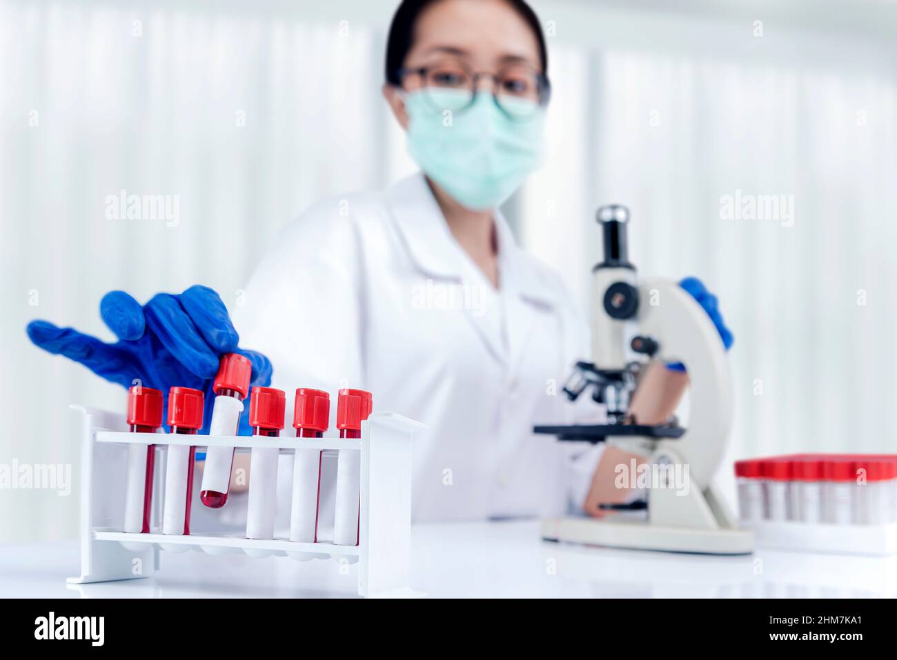 Asian researcher woman with face mask and glasses taking the medical tube from the rack on the lab Stock Photo