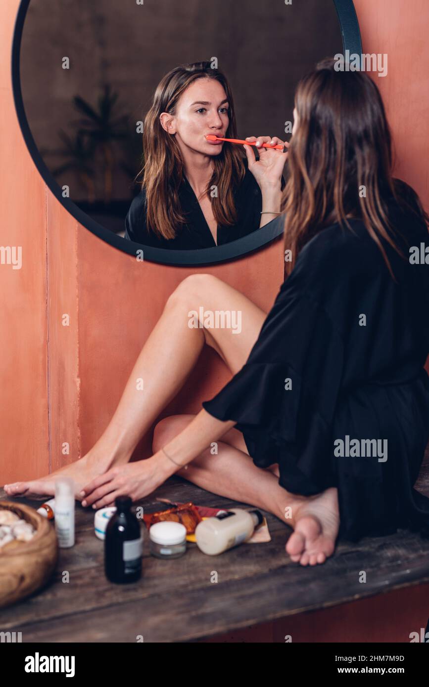 Woman brushing her teeth in the evening in front of the mirror. Stock Photo