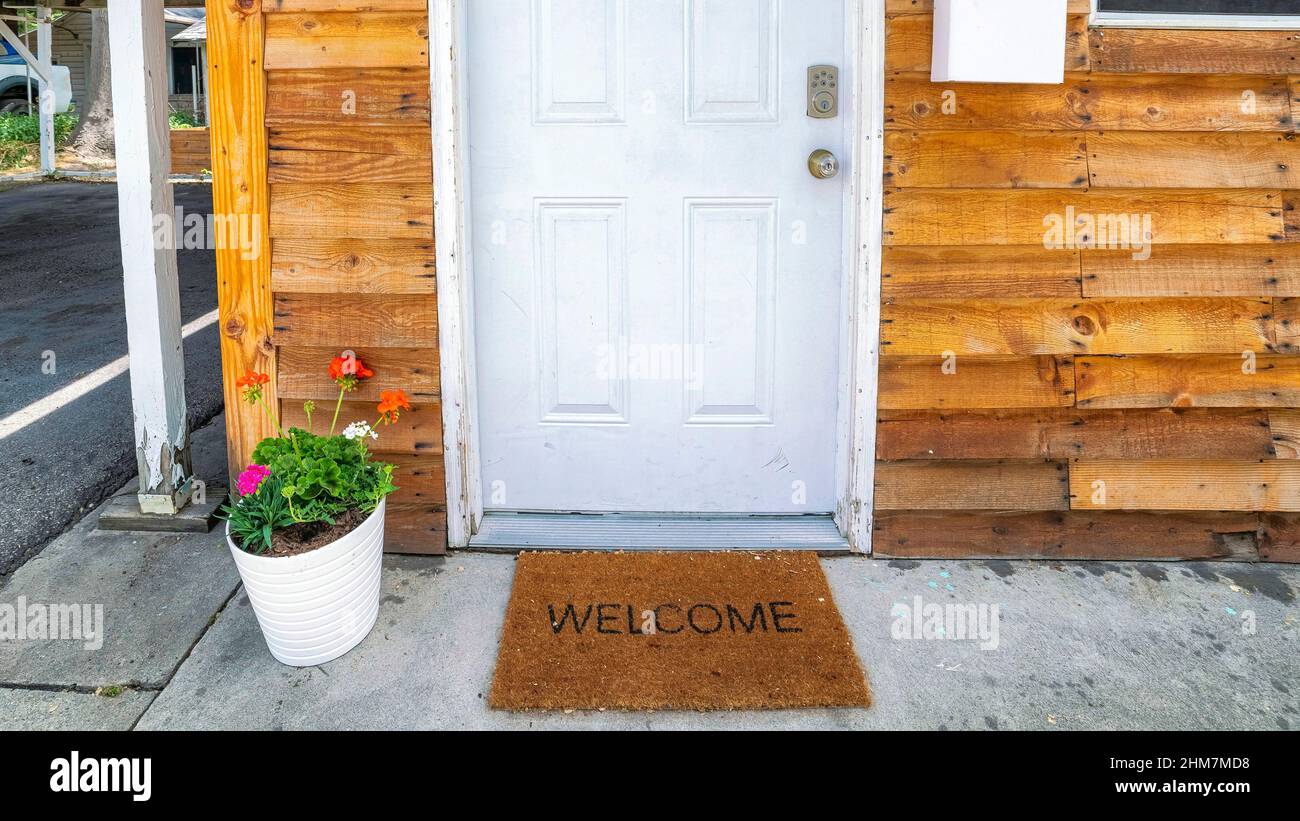 Panorama White front door decorated with flowers on a pot and doormat with welcome sign Stock Photo