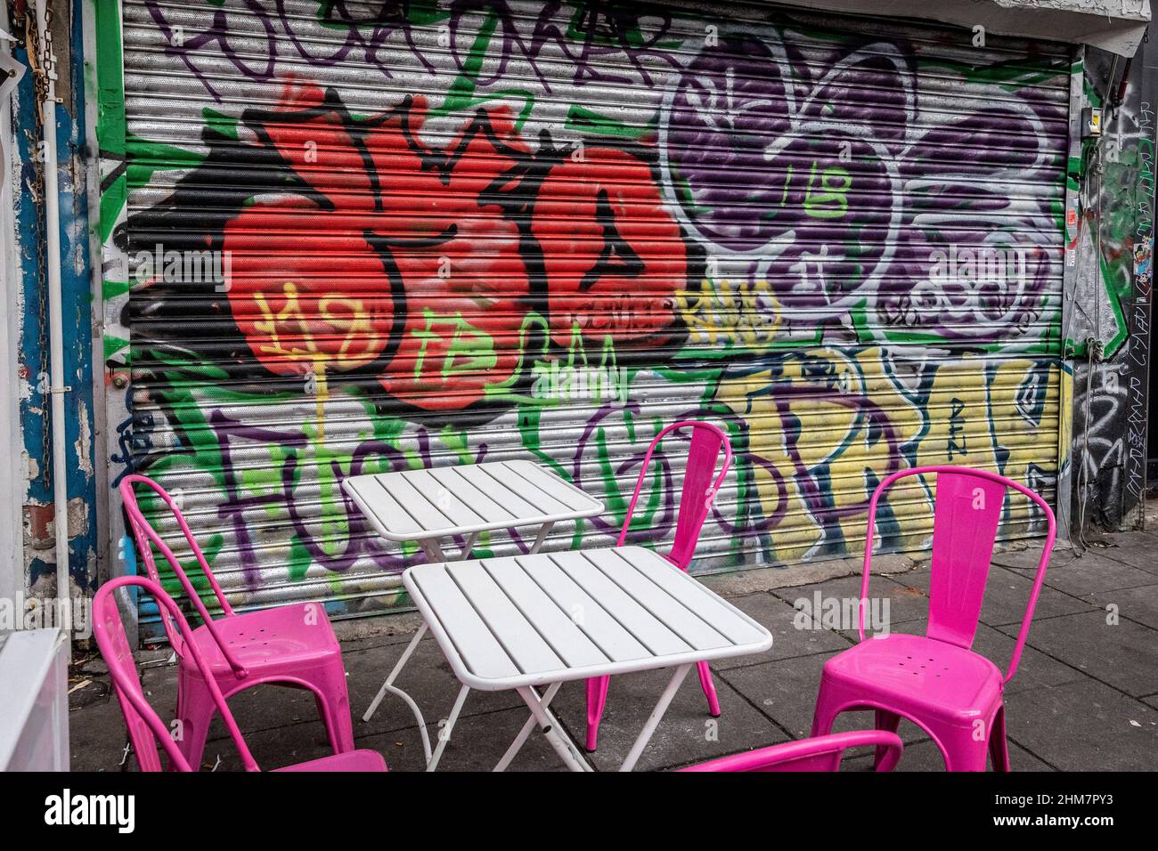 Street art on closed security shutters at cafe in Camden Town London , deserted with no customers, empty chairs. Stock Photo