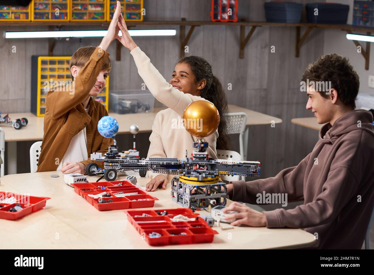 Group of teenage kids high fiving while enjoying building robots in engineering class at school, copy space Stock Photo