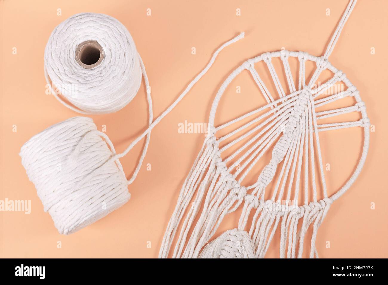 Rolls of cotton macrame cord and finished wall hanging object on beige background Stock Photo