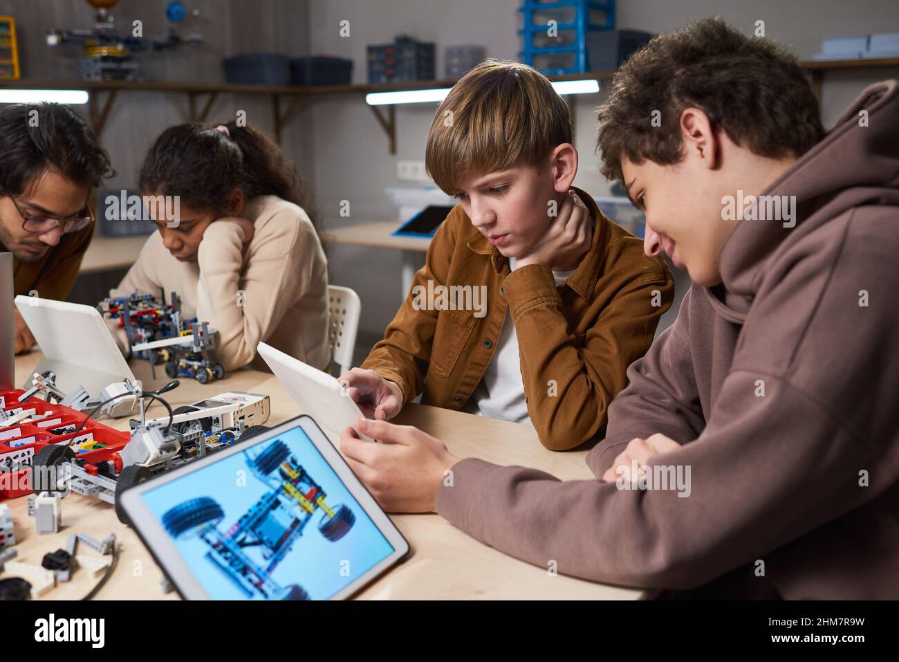 Diverse group of children using digital tablets while programming robots in engineering class at modern school Stock Photo
