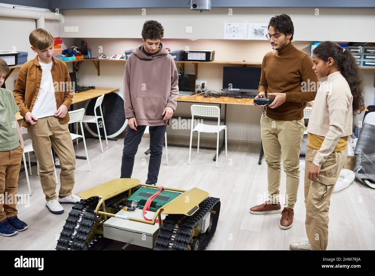 Full length portrait of diverse group of teens operating remote control robot in engineering class at school Stock Photo