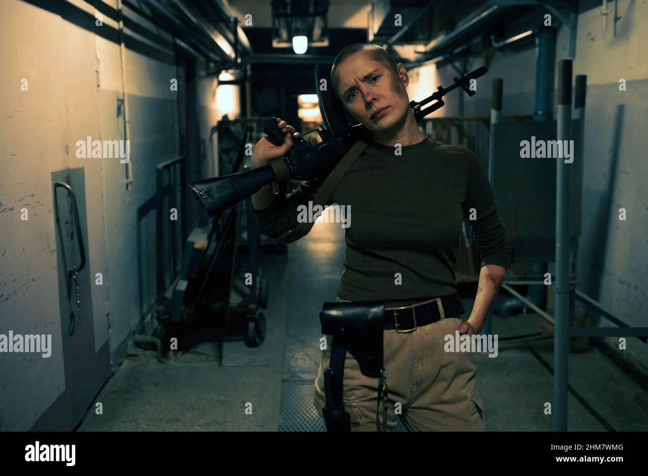 Front view portrait of tough female fighter with big gun looking at camera while standing in dark industrial hallway, copy space Stock Photo