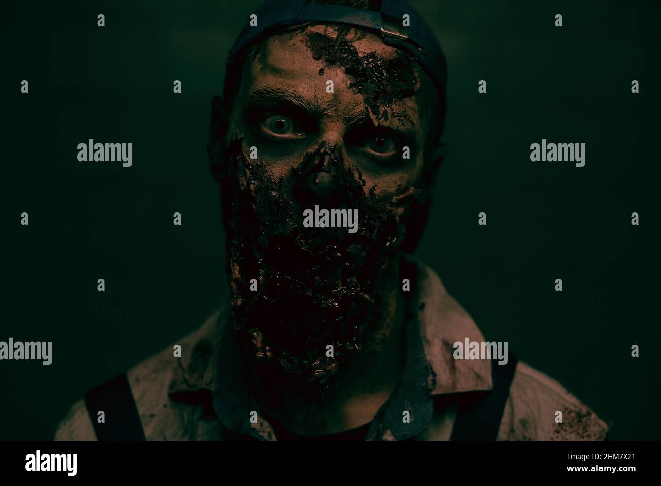 Close up shot of creepy zombie with bloody face looking at camera in dark horror setting, copy space Stock Photo