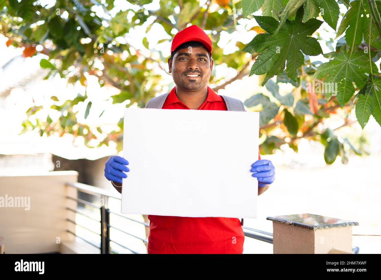 Happy smiling delivery boy with white sign board looking at camera - concept of free and fast home courier service promotion and advertisement Stock Photo