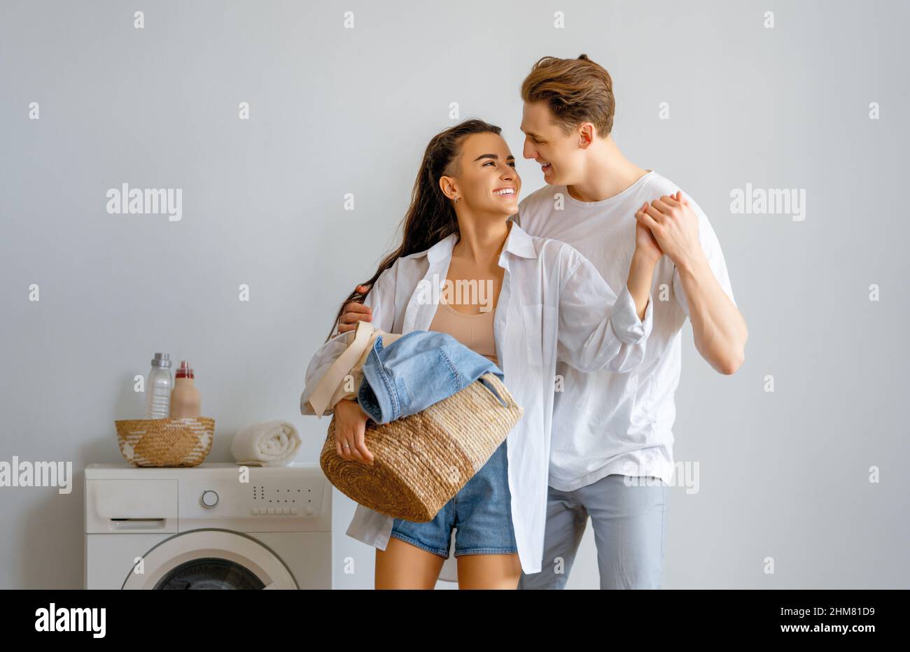 Beautiful young loving couple is smiling while doing laundry at home ...
