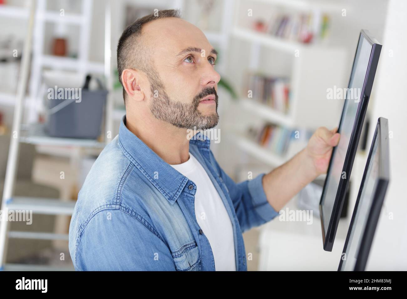 man hanging picture frames in his home Stock Photo Alamy