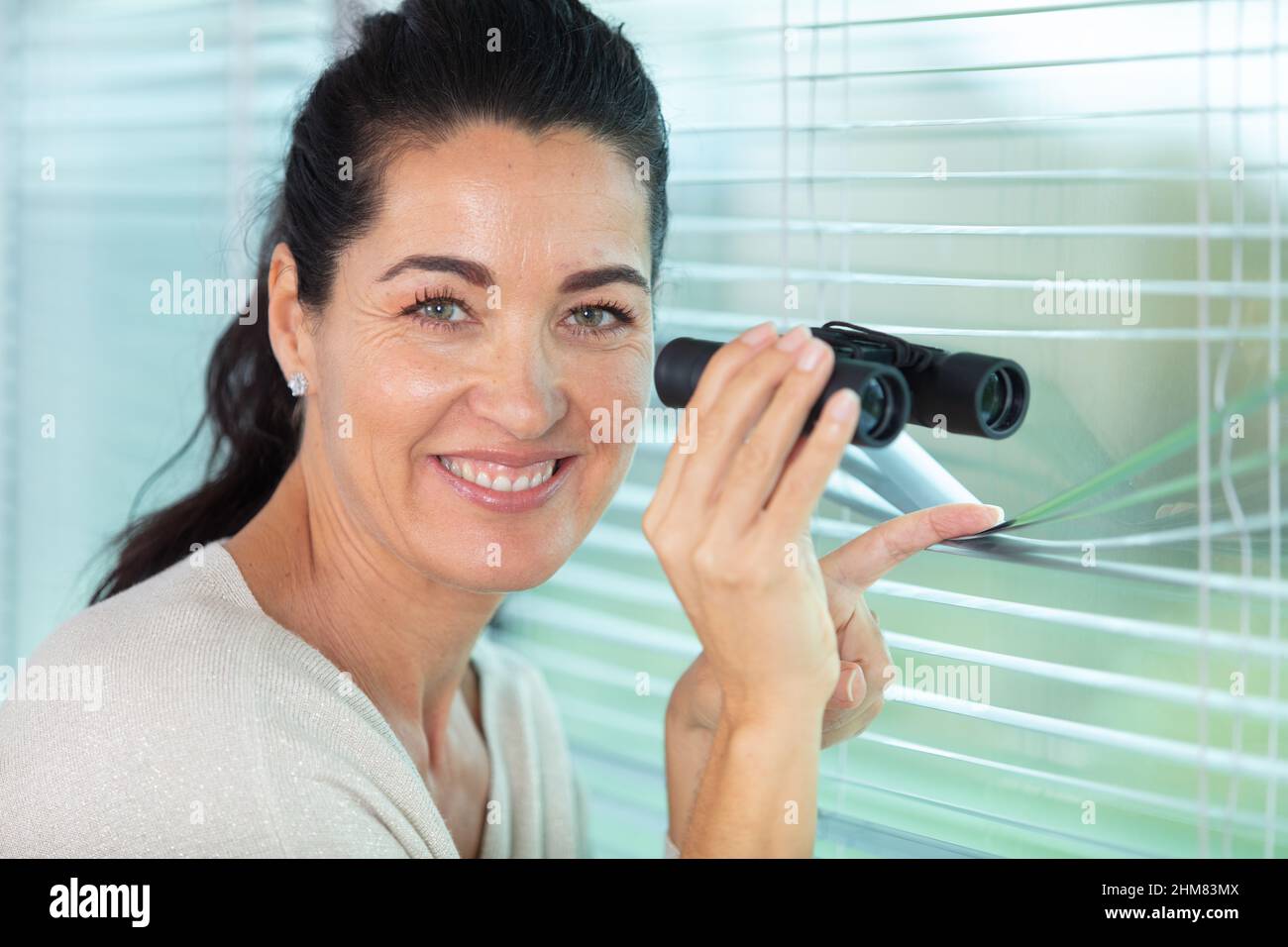 nosy woman peering through some blinds Stock Photo