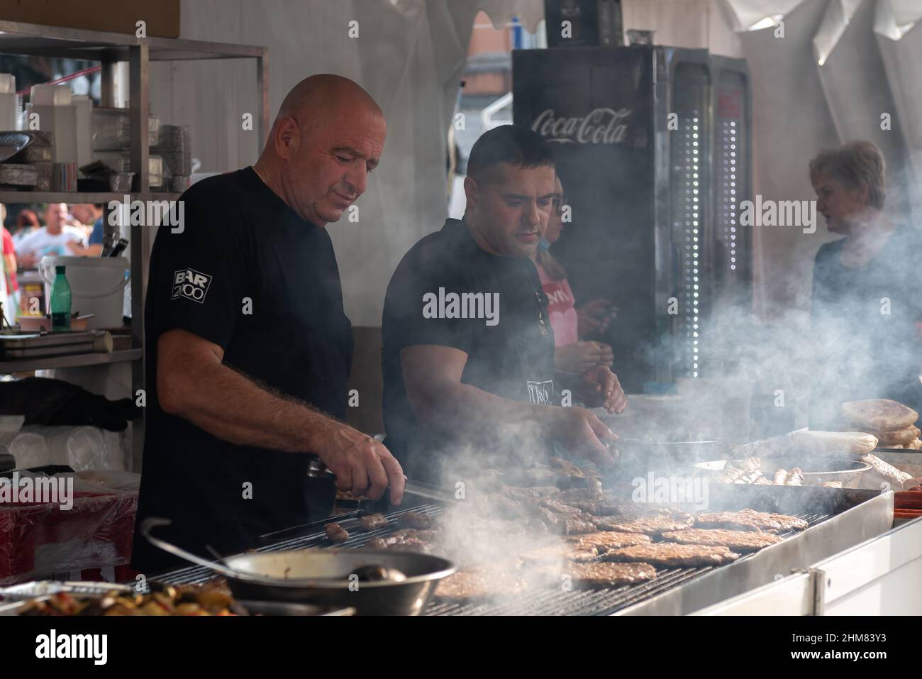 People cooking grilled meat during a city festival. Street food concept. Gorizia city, Friuli Venezia Giulia, Italy. Stock Photo