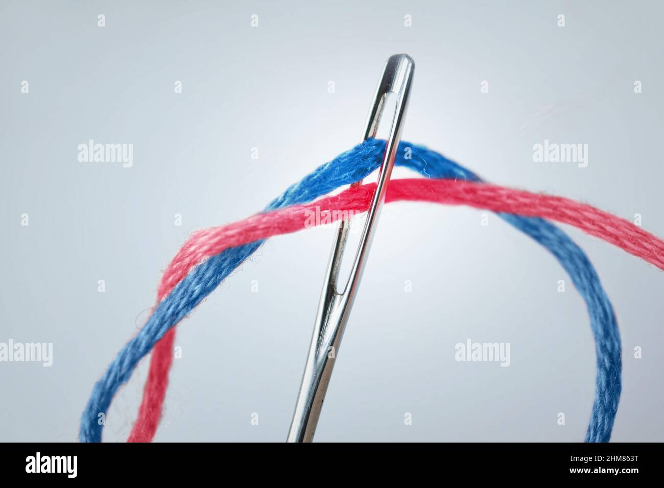 Close-up of sewing needle eye with pink and blue thread - Concept of diversity and gender issues Stock Photo