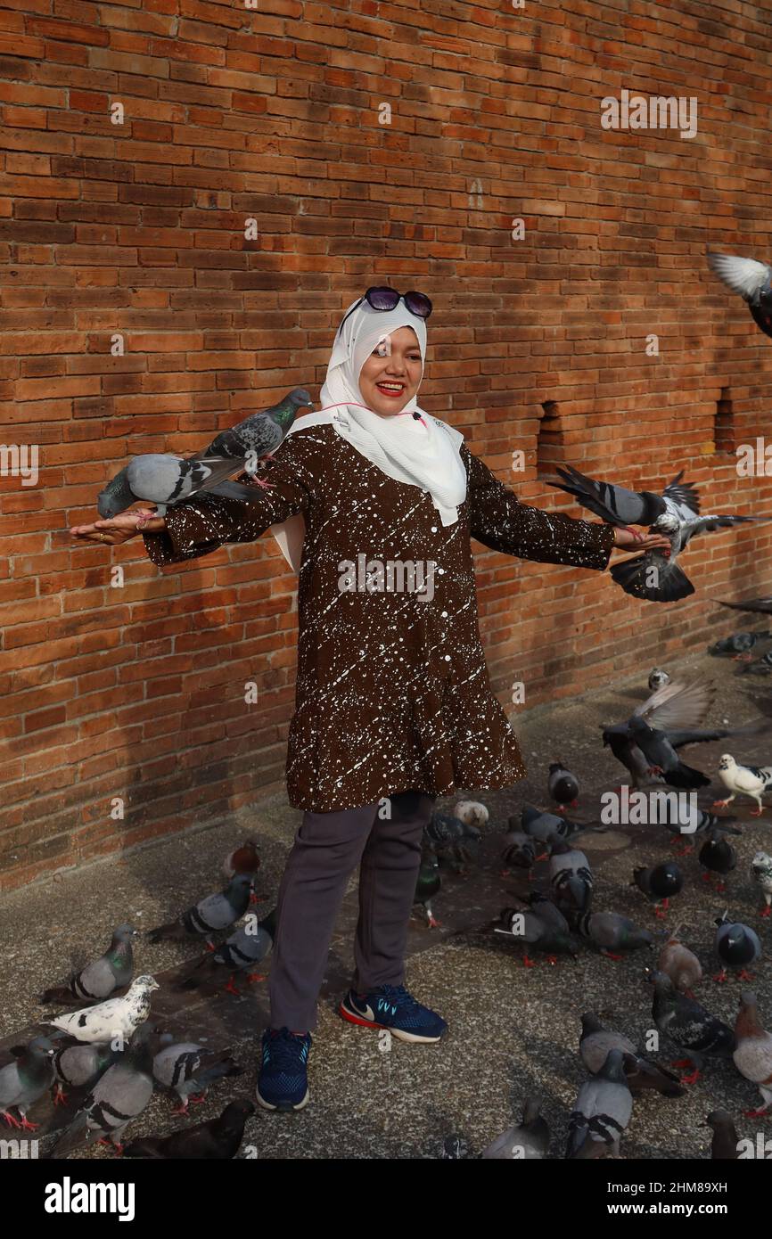 Thai Muslim woman smiling and feeding the Pigeons in front of the Tha Phae gate, Chiang Mai, Thailand Stock Photo