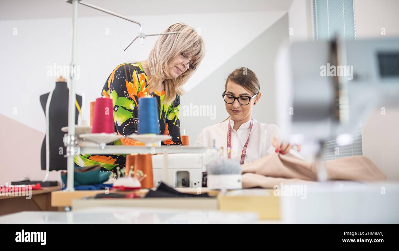 Two generations of female tailors cooperate at work in the small workshop. Stock Photo
