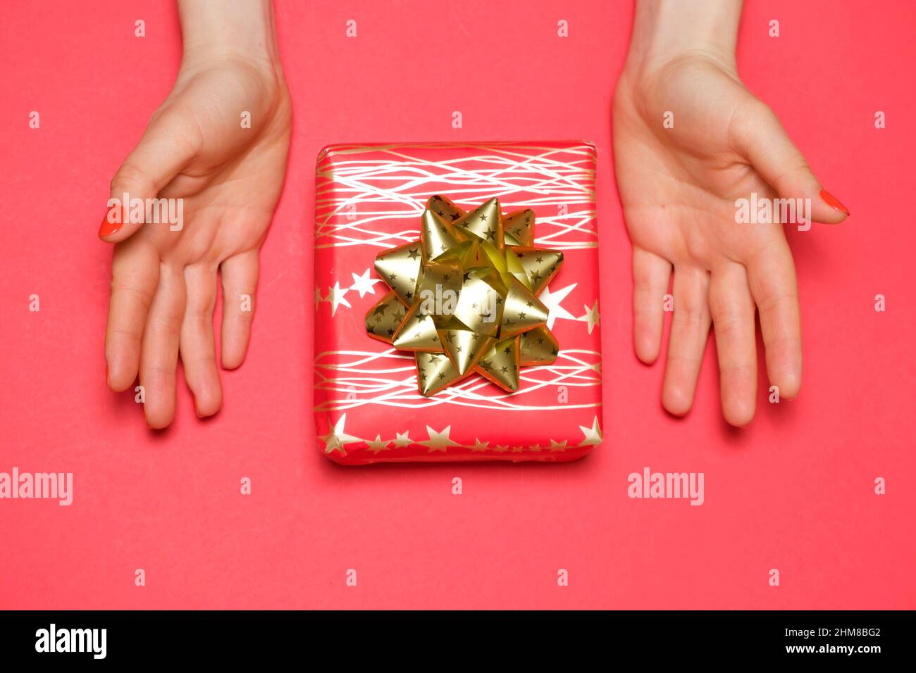 Beautiful red gift box with bow in women's hands, top view, copy space for text. Stock Photo