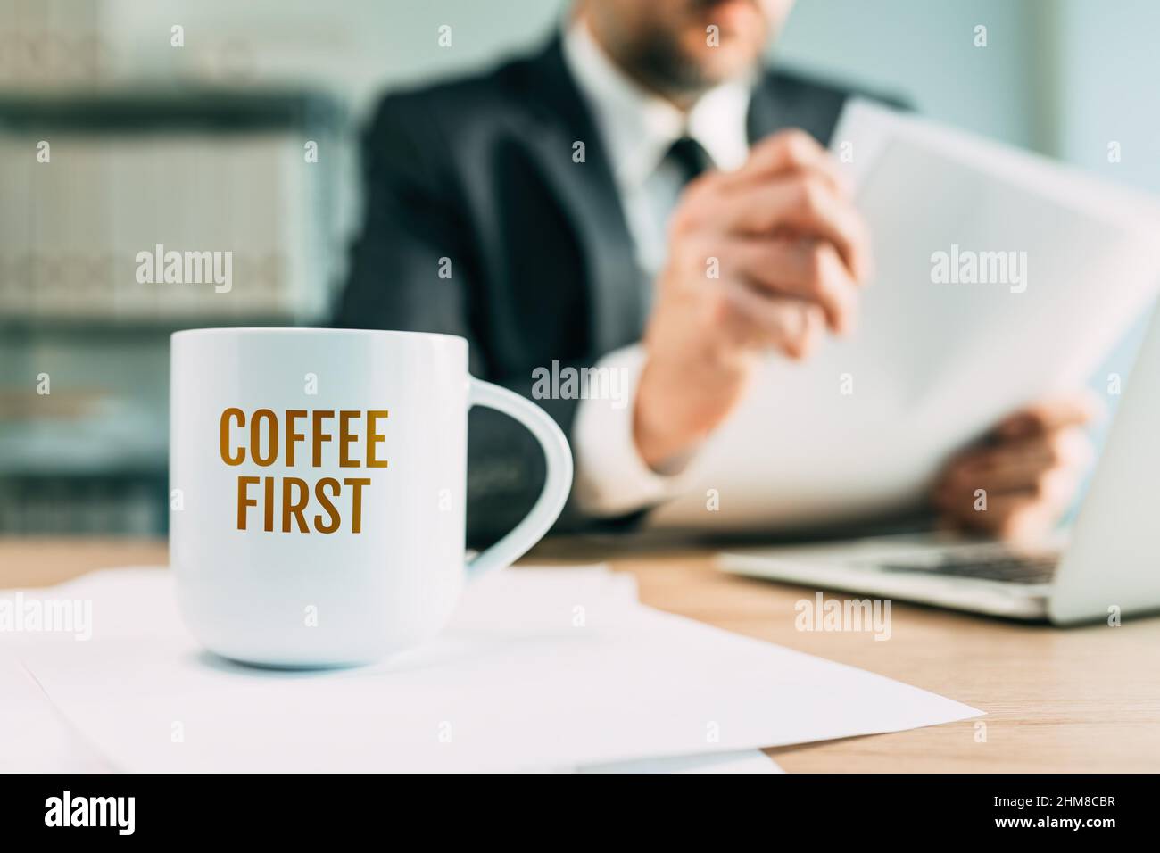 Coffee first quote on white mug in business office, businessman reading financial report in the background, selective focus Stock Photo