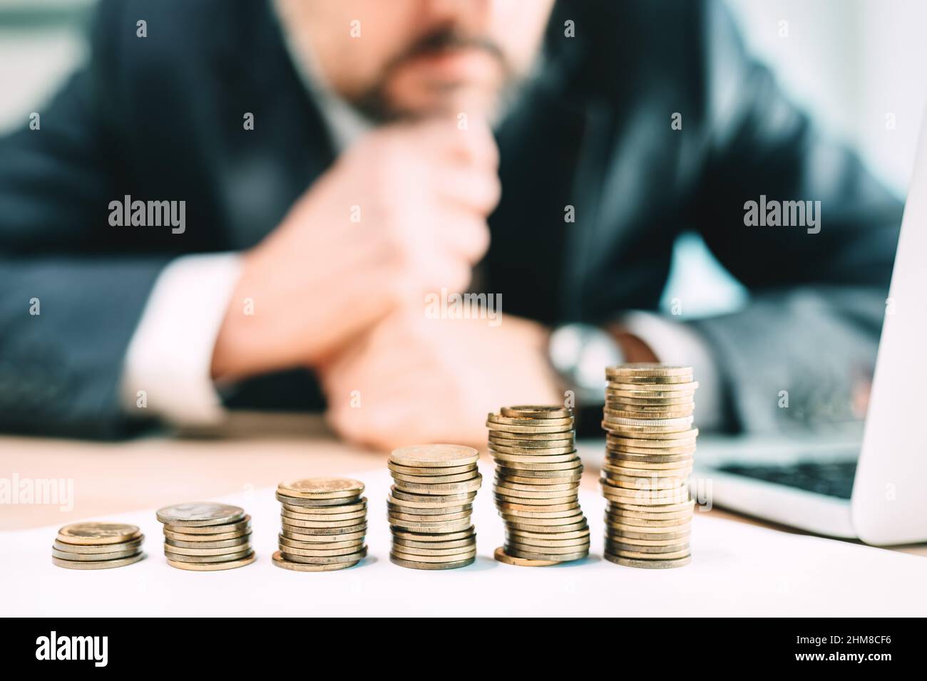 Investment planning concept, businessman looking at coin stack at office desk, selective focus Stock Photo