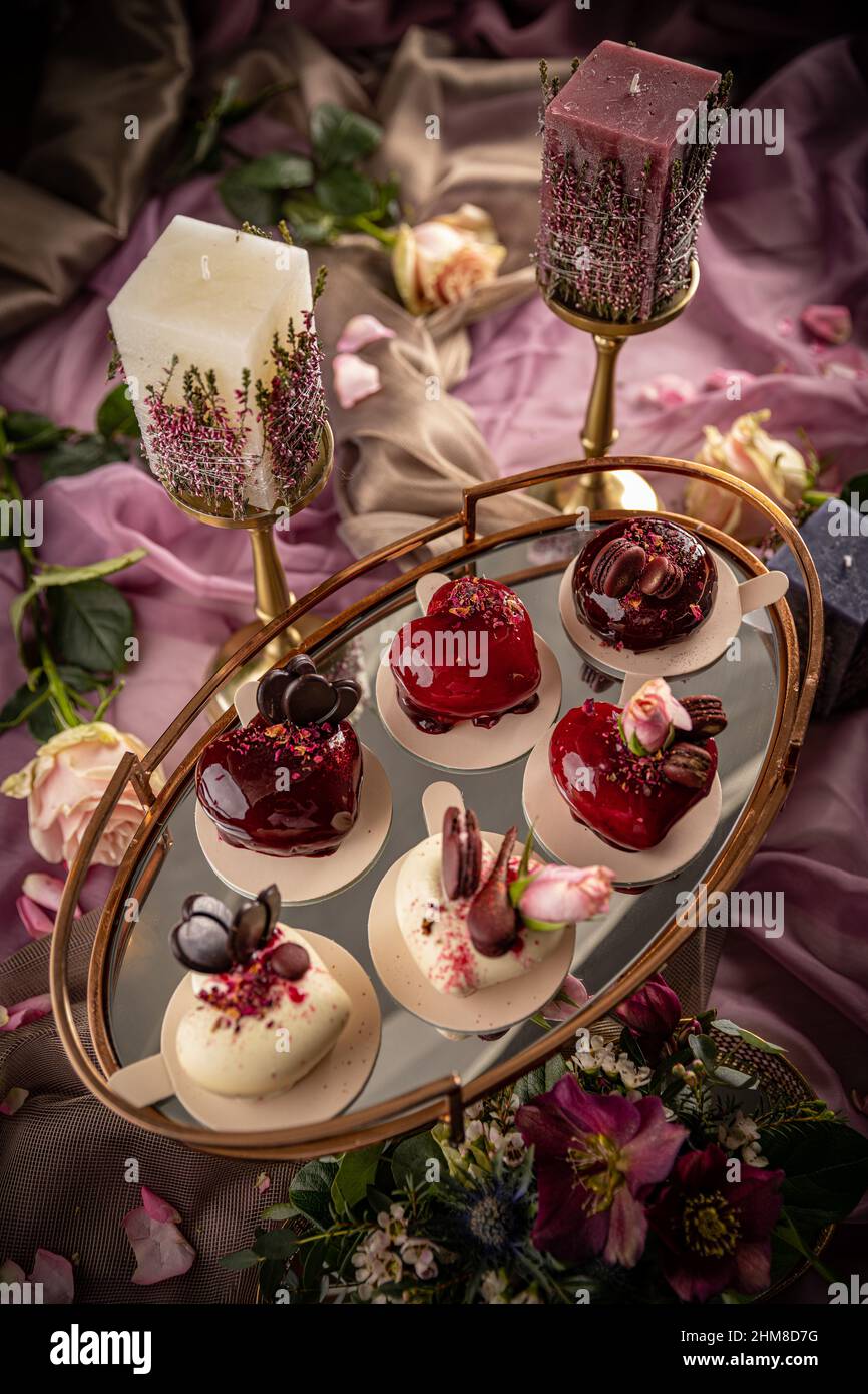 Still life of heart shaped mini cakes decorated with rose, chocolate or macarons Stock Photo