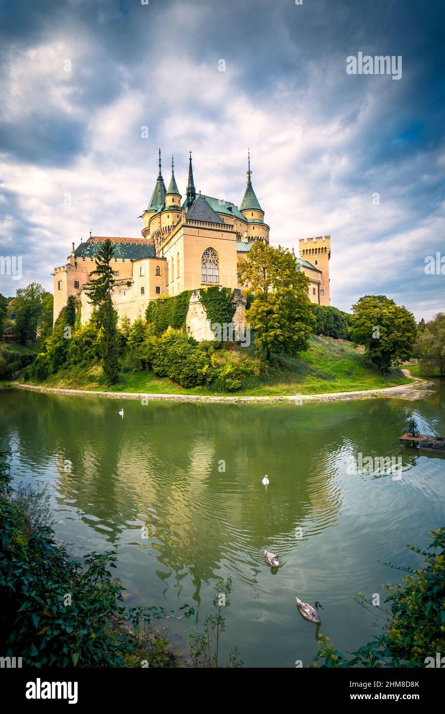 Medieval castle Bojnice over lake with swans. Dramatic illuminated blue sky with clouds. Central Europe, Slovakia. Stock Photo