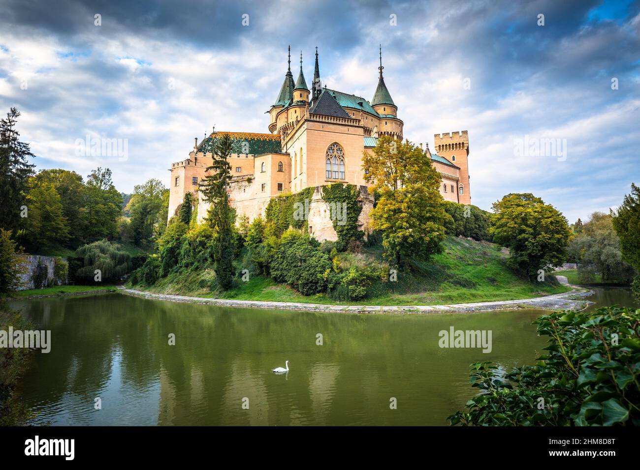 Medieval castle Bojnice over lake with swan. Dramatic illuminated blue sky with clouds. Central Europe, Slovakia. Stock Photo