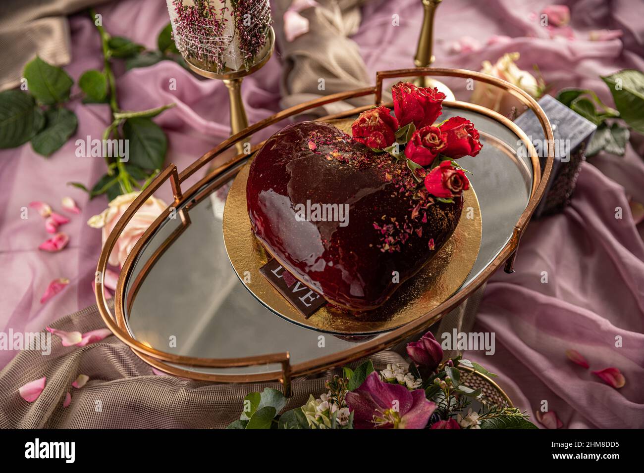 Heart shaped cake with red mirror glaze, rose on top as decoration. Stock Photo