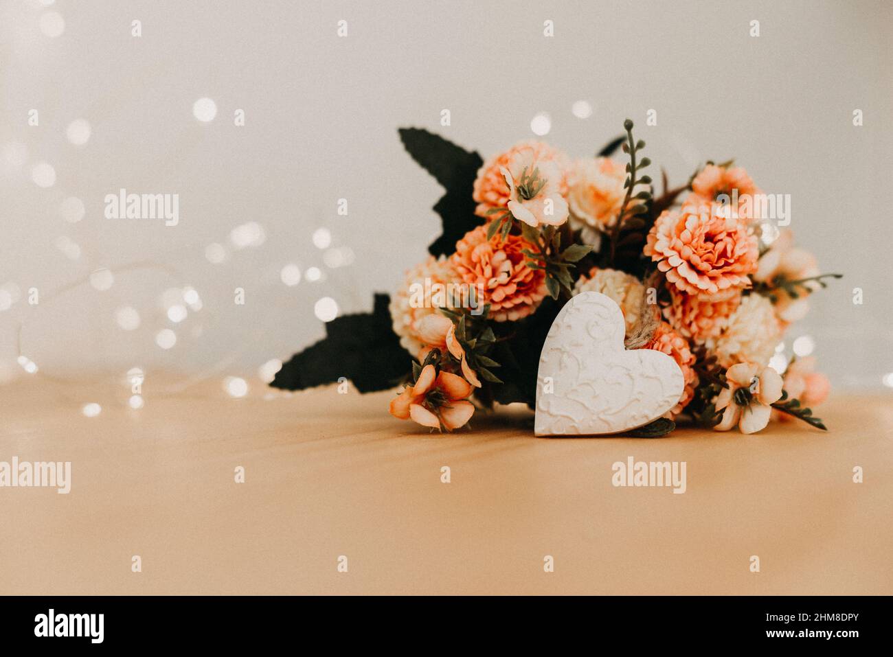 wooden table with a bouquet of flowers and a white heart and bokeh lights around it. Stock Photo