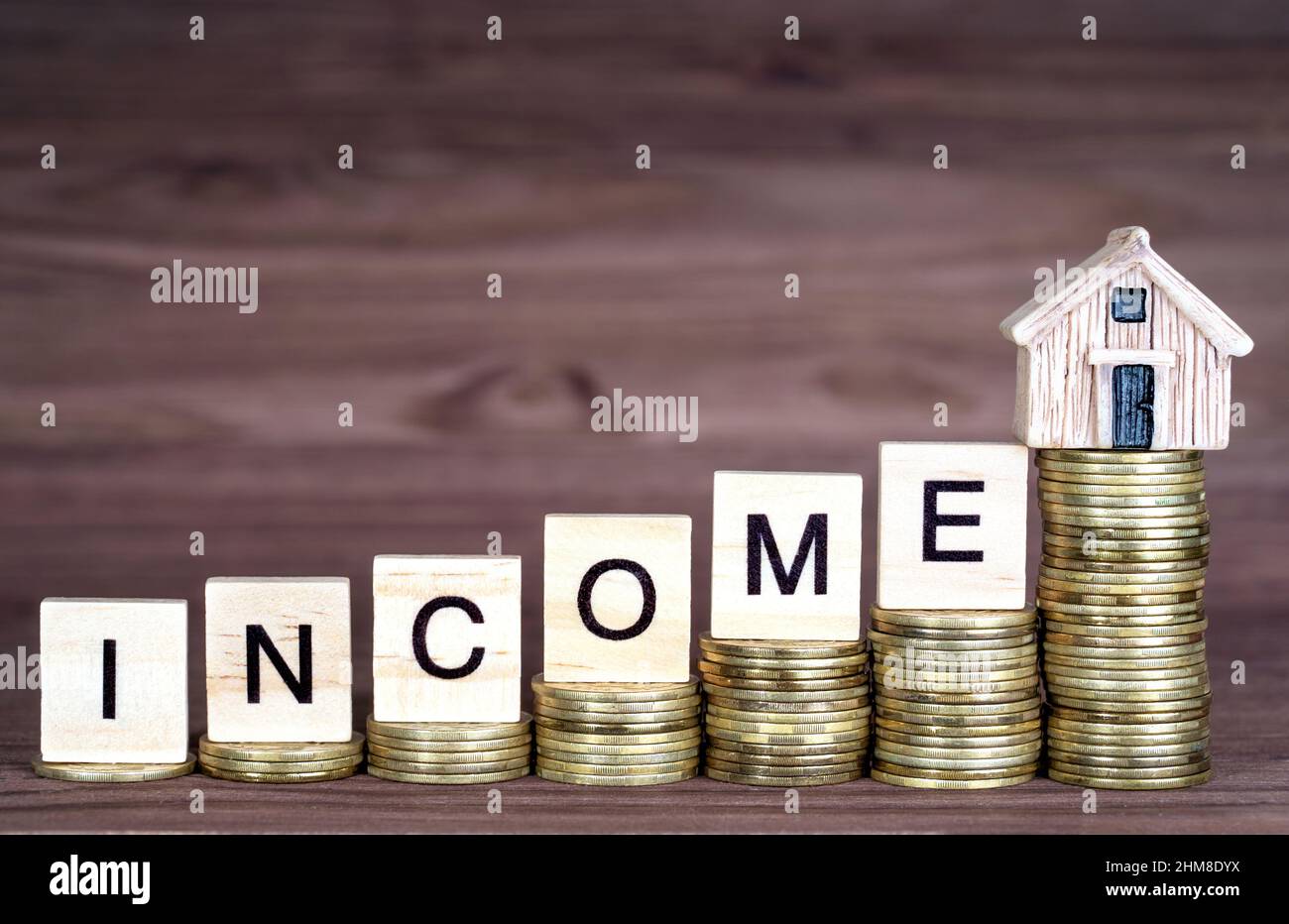 Word INCOME made from wooden letter blocks and a small toy house placed on ascending coins stacks. Increasing income for a mortgage deposit. Stock Photo