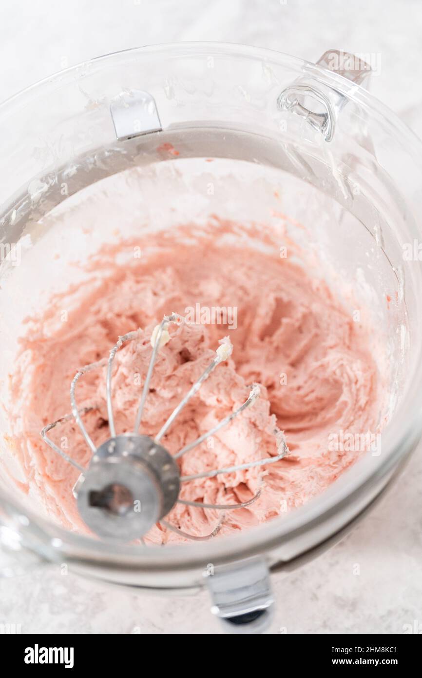 Whipping strawberry buttercream frosting in a standalone electric mixer with a whisk attachment
