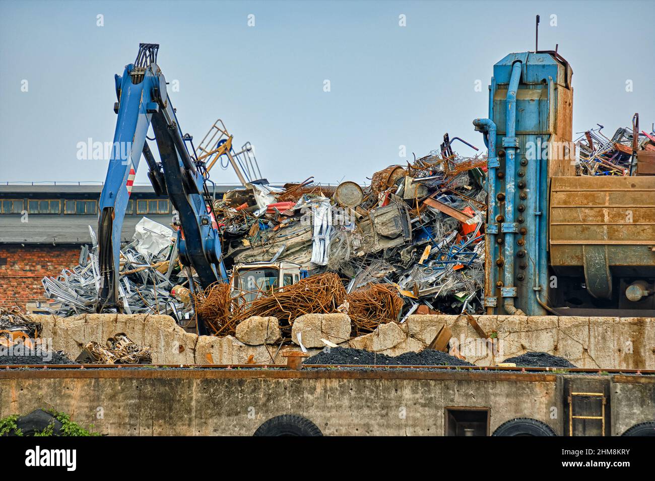 Close view of backhoe loader and big pile of construction debris in river port in overcast day. Metal and concrete waste recycle. Stock Photo