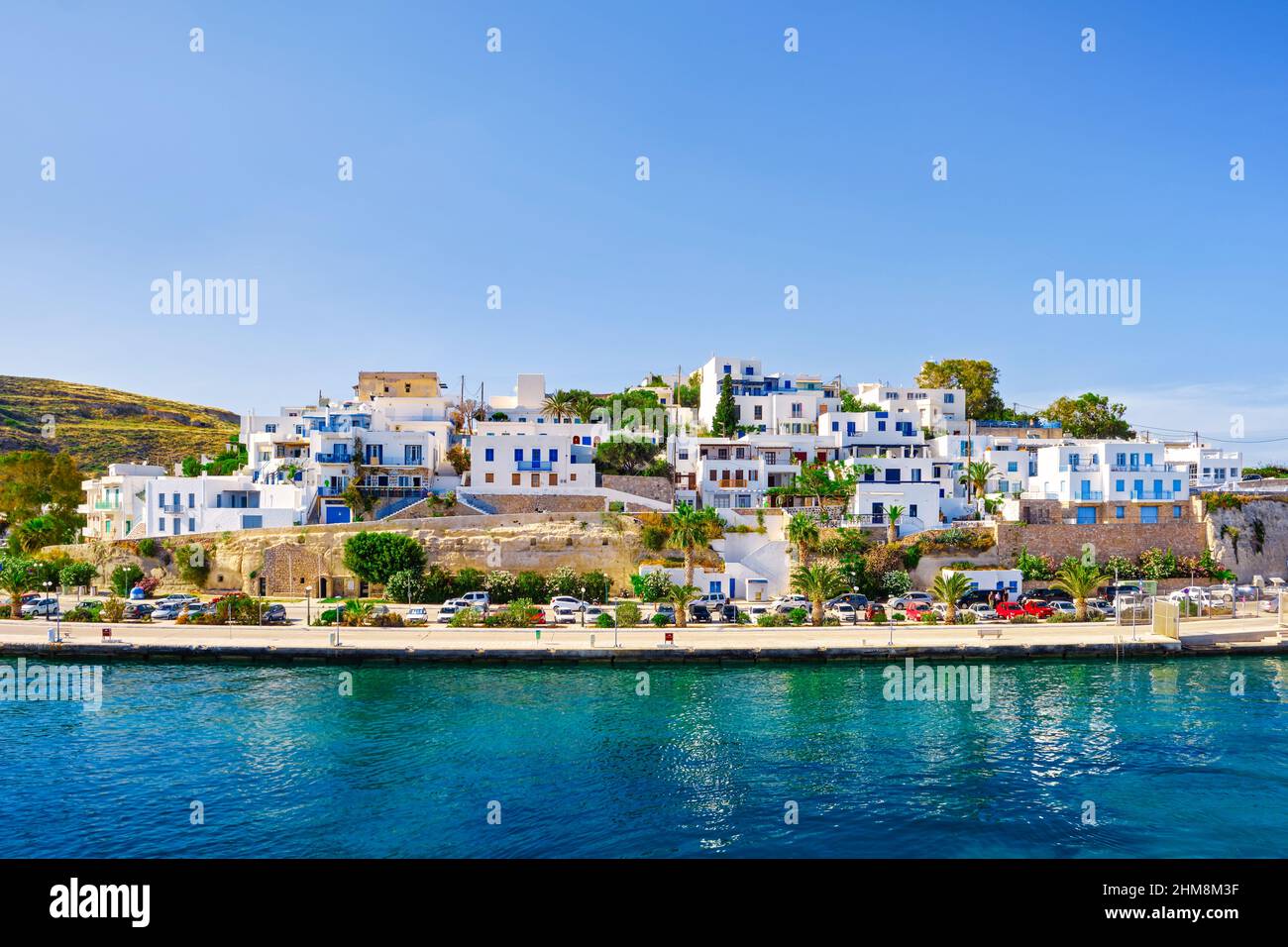 Beautiful summer day, sunshine in typical marina of Greek island. Whitewashed houses by waterfront. Mediterranean vacations. Milos, Cyclades, Greece. Stock Photo