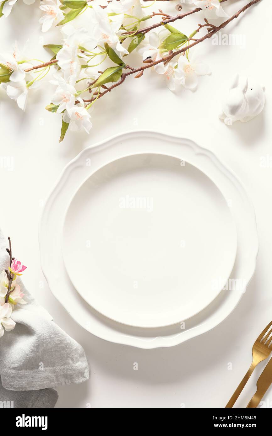 Easter festive dinner with golden eggs, festive tableware and flowers on white background. Top view. Festive tablescapes. Vertical format. Stock Photo