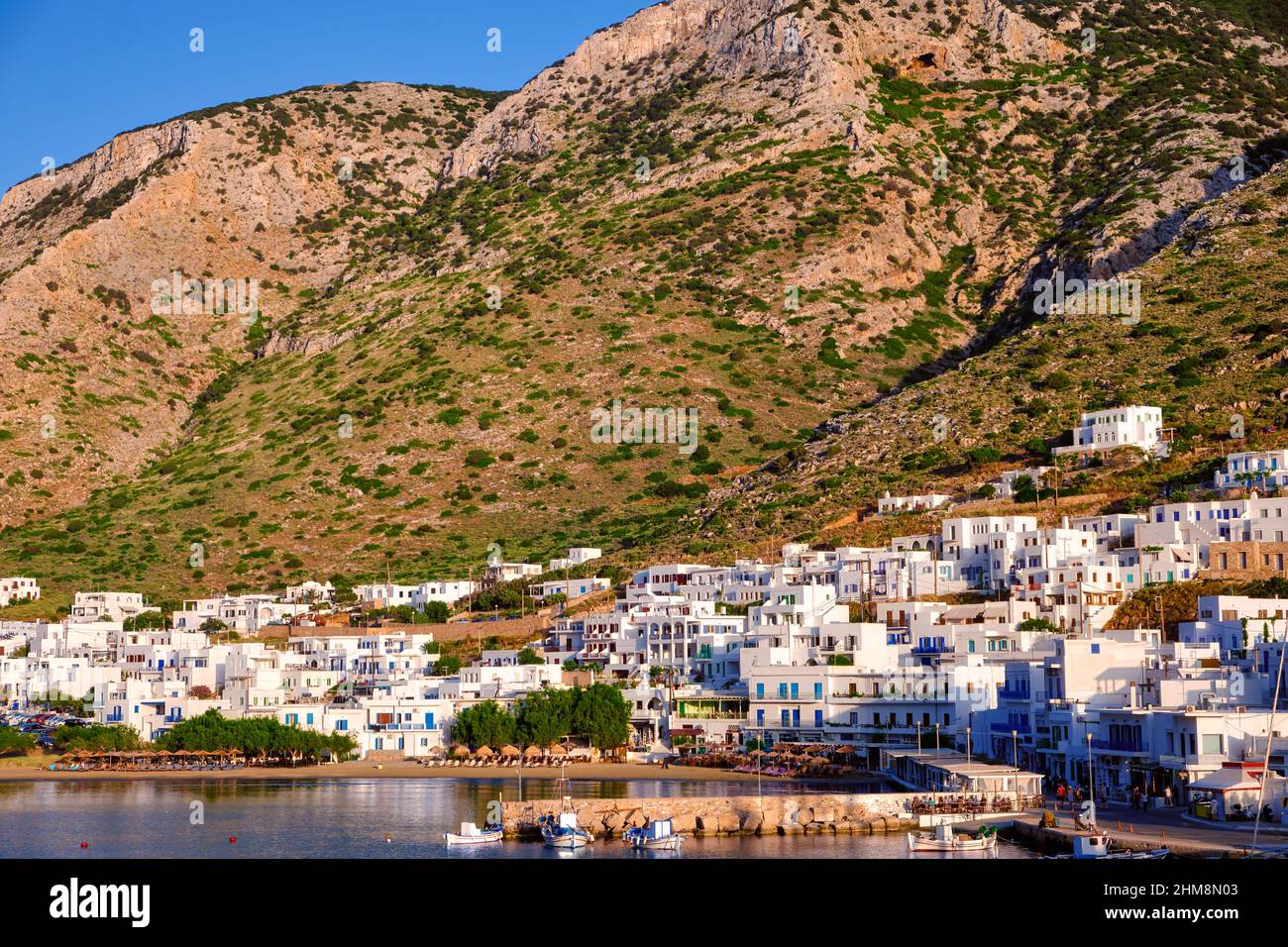 Beautiful view of Mediterranean island at sunset. Whitewashed houses, hills, clear sky, blue sea waters, beaches. Small Greek village of Milos, Greece Stock Photo