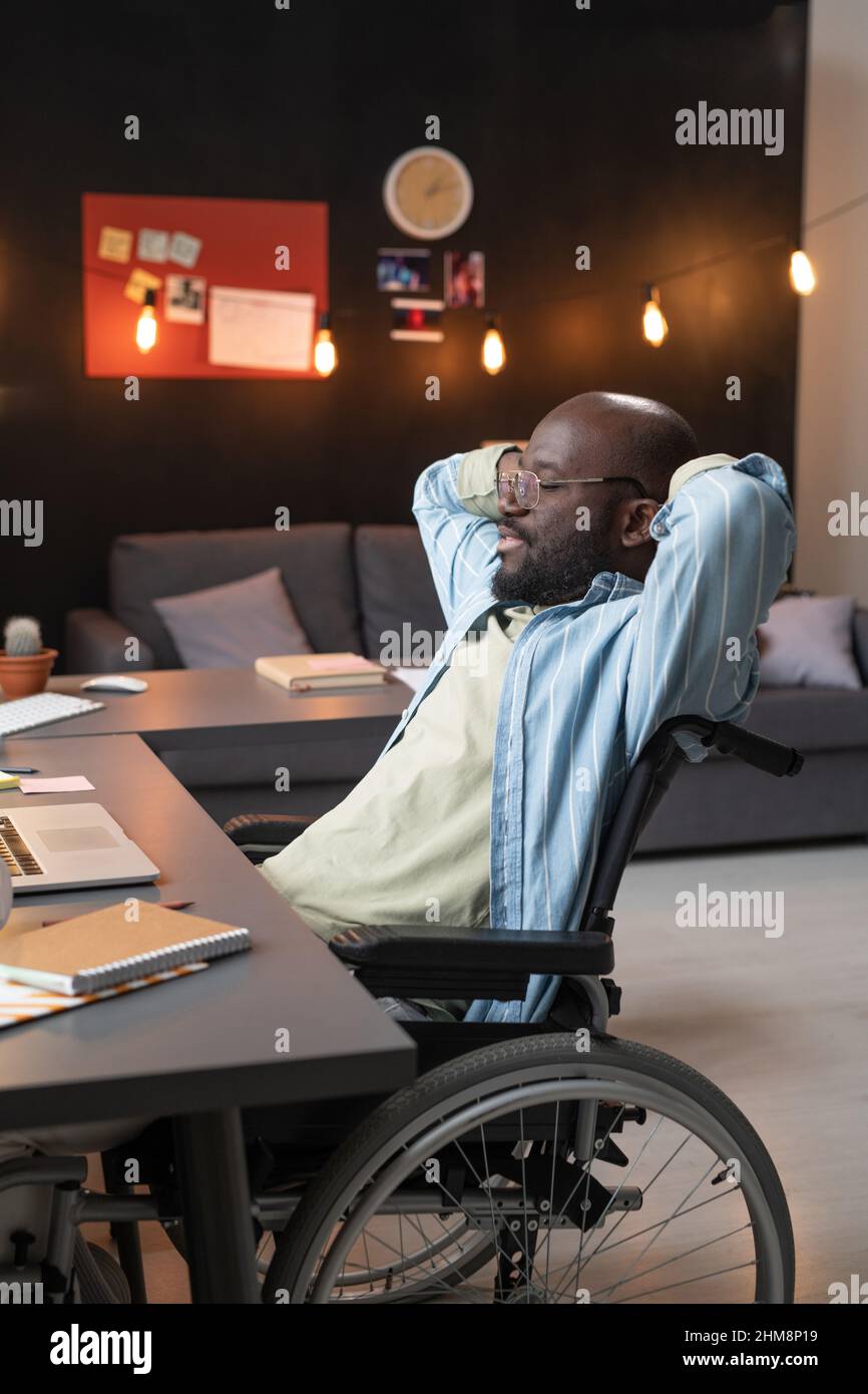 African man sitting on wheelchair at his workplace, he resting after work at home Stock Photo