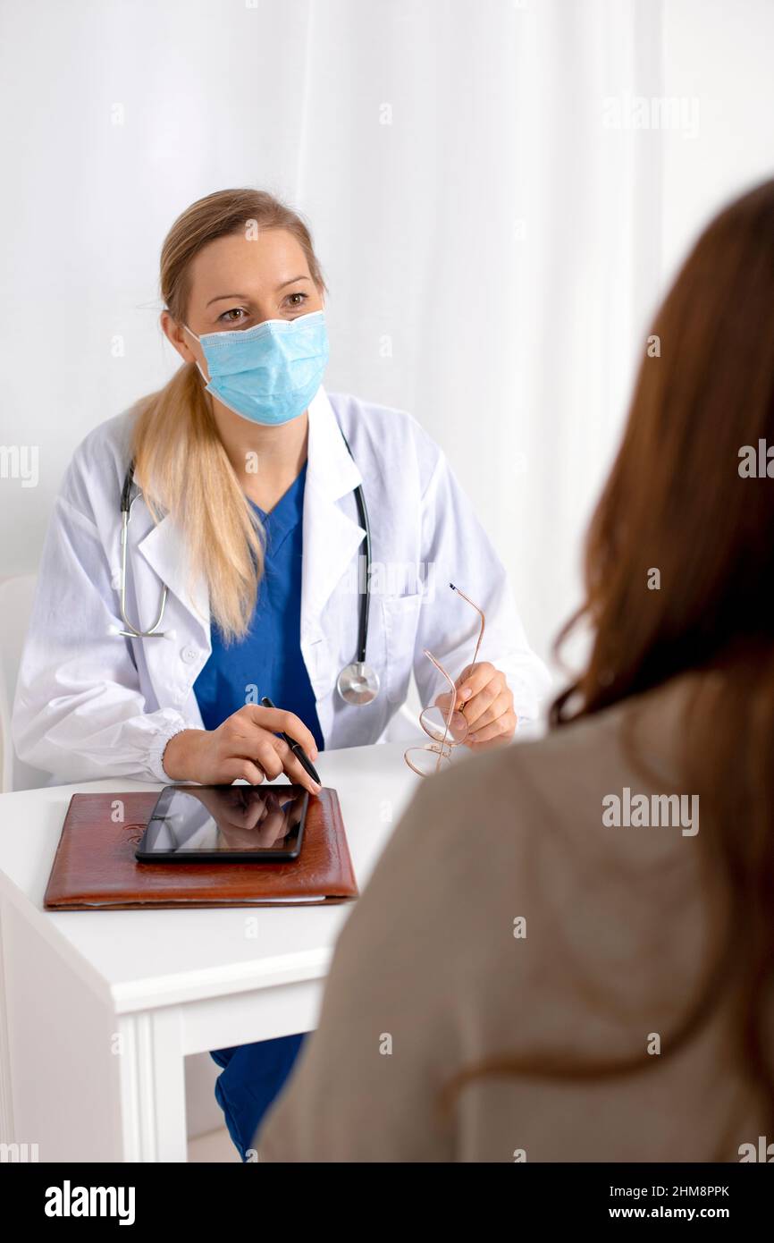 Young brunette woman having consultation at doctor office during coronavirus and flu outbreak. Female doctor wearing facemask. Virus protection. Covid Stock Photo