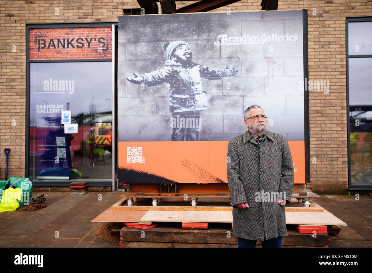 John Brandler, the owner of Season's Greetings by street artist Banksy,  observes the artworks removal from a retail unit at Ty'r Orsaf, Port  Talbot, prior to its journey to a temporary storage