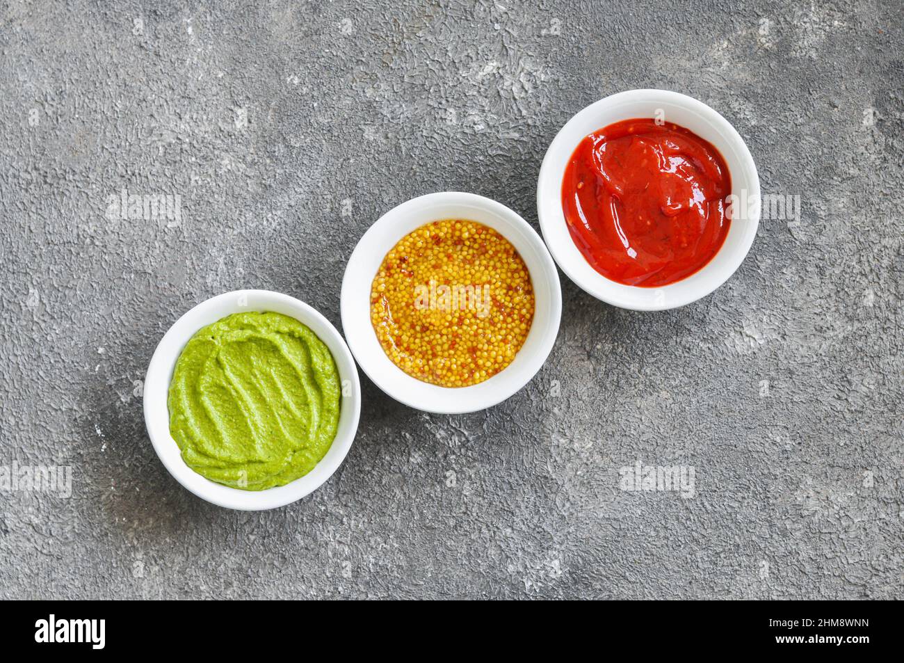 Assorted sauces, french mustard, ketchup and guacamole on a grey background. Top view. Stock Photo